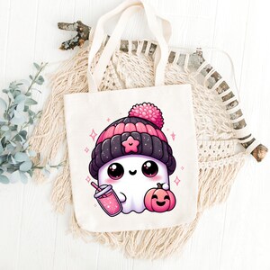 Peut inclure: Un sac fourre-tout blanc avec un adorable fant&ocirc;me de dessin anim&eacute; portant un bonnet rose et noir, tenant une boisson rose et une petite citrouille orange. Le fant&ocirc;me a de grands yeux et une expression joyeuse.