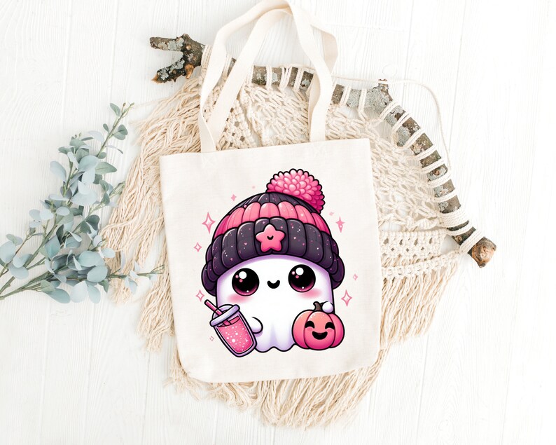 Peut inclure: Un sac fourre-tout blanc avec un adorable fant&ocirc;me de dessin anim&eacute; portant un bonnet rose et noir, tenant une boisson rose et une petite citrouille orange. Le fant&ocirc;me a de grands yeux et une expression joyeuse.
