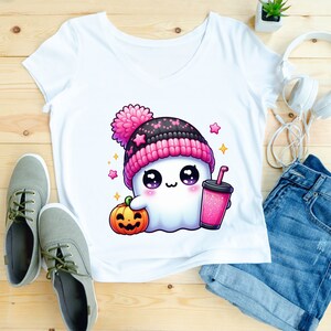 Peut inclure: T-shirt blanc avec un mignon fant&ocirc;me de dessin anim&eacute; portant un chapeau rose et noir, tenant une tasse rose et blanche avec une paille et une petite citrouille orange. Le fant&ocirc;me a de grands yeux et un petit sourire.