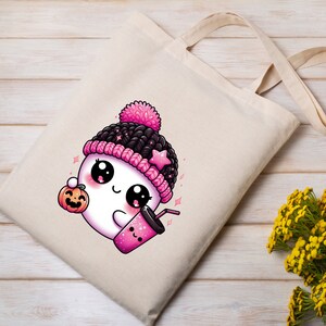 Peut inclure: Un sac en toile blanc avec un fant&ocirc;me de dessin anim&eacute; rose et noir portant un chapeau rose et noir, tenant une citrouille et une tasse rose avec une paille. Le fant&ocirc;me a de grands yeux et un sourire mignon.