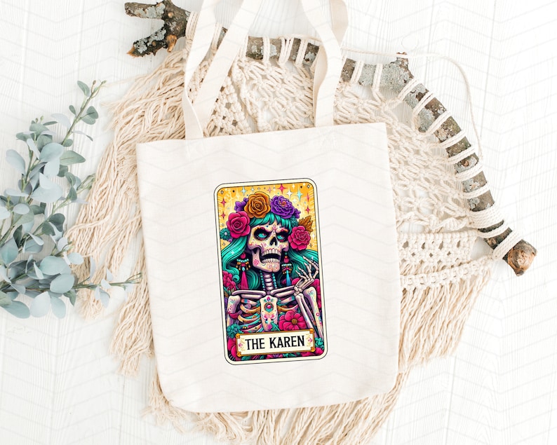 May include: A white tote bag featuring a colourful illustration of a skeleton wearing a flower crown. The illustration is in the style of a tarot card and says "The Karen" at the bottom.