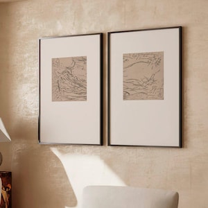 May include: Two framed rectangular wall art pieces featuring abstract brown line drawings on a light background, displayed side by side. Each piece is enclosed in a thin black frame with a wide white mat, showcasing minimalist sketches.