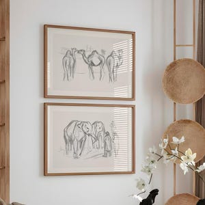 May include: Two framed pencil sketches of animals hang on a white wall. The top frame features camels, and the bottom frame depicts elephants. A modern dining table with chairs and decorative items completes the scene.