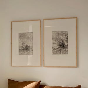 May include: A bedroom scene with a bed dressed in white bedding and a black striped duvet cover. Two framed landscape art prints are mounted above the bed. Brown throw pillows and a rust-coloured throw blanket add warmth to the neutral colour palette.