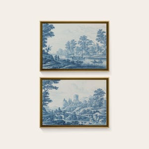 May include: Two rectangular wall art prints featuring blue and white landscape illustrations in gold frames. The top print shows a river scene with boats and buildings. The bottom print depicts a stone bridge, a castle tower, and a river landscape.