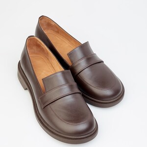 Classic women’s loafers crafted from smooth brown leather, featuring a timeless slip-on design with a rounded toe and low heel. The interior is lined with soft leather for comfort, while the sturdy sole ensures durability and everyday wear. Perfect for pairing with casual, office, or smart-casual outfits, these versatile loafers offer a blend of elegance, comfort, and classic style for any wardrobe.
