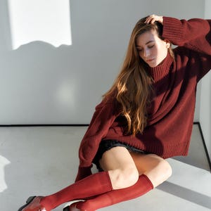 Peut inclure: Une personne porte un pull &agrave; col roul&eacute; bordeaux, un short noir et des chaussettes hautes. La personne porte &eacute;galement des chaussures en cuir bordeaux &agrave; lacets. La tenue est monochrome.