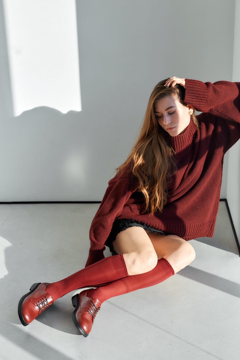 Peut inclure: Une personne porte un pull &agrave; col roul&eacute; bordeaux, un short noir et des chaussettes hautes. La personne porte &eacute;galement des chaussures en cuir bordeaux &agrave; lacets. La tenue est monochrome.