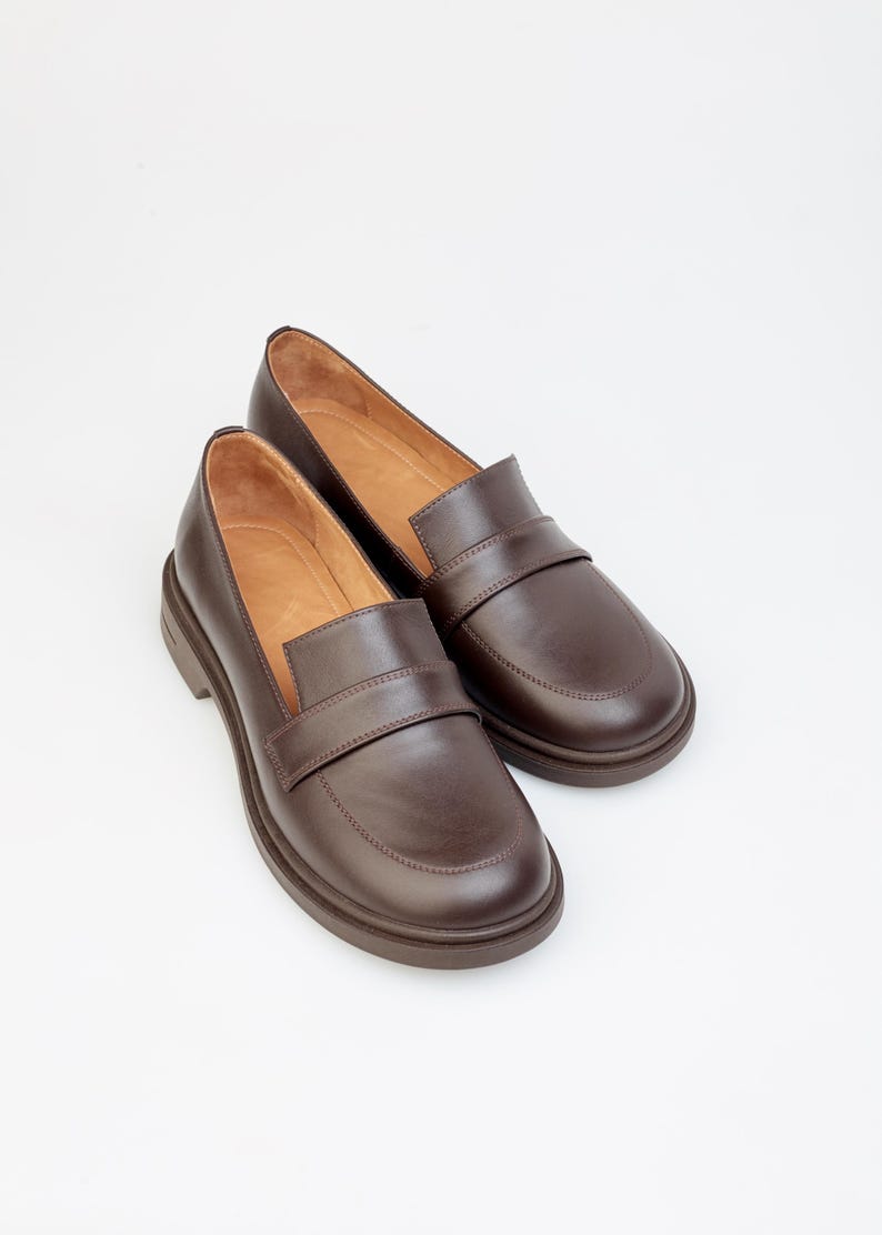Classic women’s loafers crafted from smooth brown leather, featuring a timeless slip-on design with a rounded toe and low heel. The interior is lined with soft leather for comfort, while the sturdy sole ensures durability and everyday wear. Perfect for pairing with casual, office, or smart-casual outfits, these versatile loafers offer a blend of elegance, comfort, and classic style for any wardrobe.
