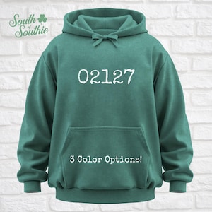 May include: A teal hoodie with a drawstring hood and a front pocket. The number "02127" is printed in white on the front. The text "3 Color Options!" is below the number. The "South Southie" logo is in the upper left corner.