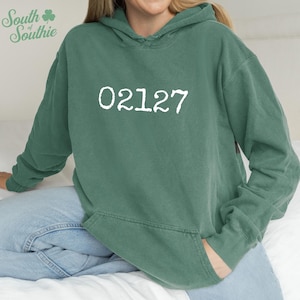 May include: A teal green hoodie with the white number sequence "02127" printed on the front. The sweatshirt has a drawstring hood and a front pocket. The sleeves are long and the material appears to be soft and comfortable.