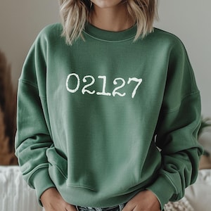 May include: A green sweatshirt with the white text "02127" across the chest. The sweatshirt has a crew neck and long sleeves. The fabric appears soft and comfortable.