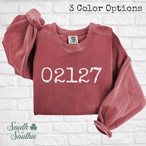 May include: A white ceramic mug with a black handle and the text "But First, Coffee" in a black, bold font. The mug is on a white surface.