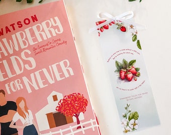 May include: A white bookmark with a red strawberry charm and a floral design. The bookmark has the text "Strawberry Fields for Never by Kate Watson".