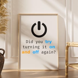 May include: A framed print with a black power button icon and the text "Did you try turning it on and off again?" in black, blue, and orange. The print is in a light wood frame.