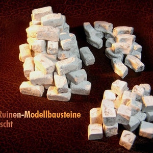 Könnte beinhalten: Mehrere Haufen kleiner, hellfarbiger, rechteckiger Modellbausteine, die verwitterten Ziegeln ähneln. Der Text "100 Ruinen-Modellbausteine gemischt" ist unten links sichtbar.