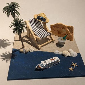 Könnte beinhalten: Eine Miniatur-Strandszene mit einem Holzliegestuhl, Strohhut, Sonnenbrille und einem Kreuzfahrtschiff. Die Szene umfasst Palmen, Muscheln und ein Schild mit der Aufschrift "Schönen Urlaub!". Eine Champagnerflasche steht in einem Eiskübel.