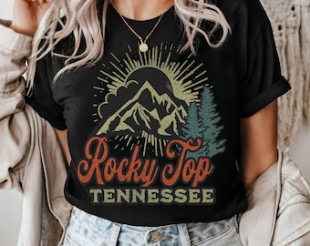 May include: Black t-shirt with a vintage-style graphic of mountains, a sun, and trees. The text "Rocky Top Tennessee" is printed in red, orange, and yellow.