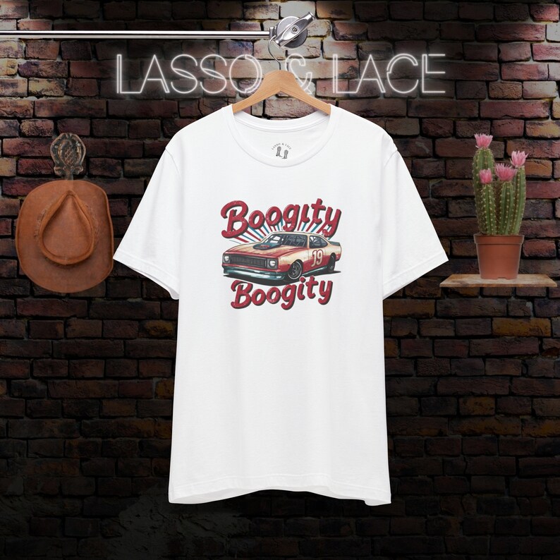 以下が含まれることがあります： 白地に赤と白のレースカーのグラフィックがプリントされたTシャツ。カーの上下に「Boogitty」の文字が書かれている。