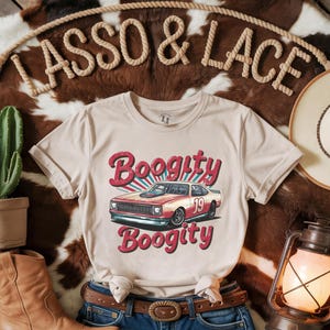 以下が含まれることがあります： ベージュのTシャツに、赤いレーシングカーのレトロなグラフィックがプリントされています。赤い文字で「Boogitty」と書いてあり、車の側面には「19」の数字が書かれています。