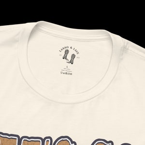 May include: A white t-shirt with a brown graphic print of the word "TEXAS" in a vintage style. The shirt has a neck label with the text "LASSO & LACE" and a pair of cowboy boots.