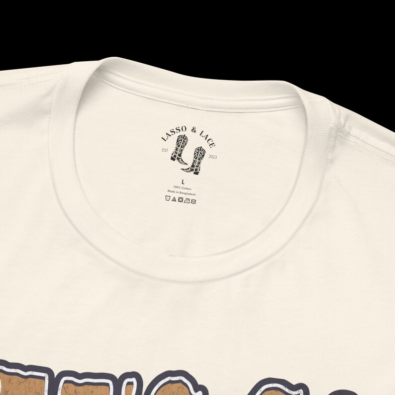May include: A white t-shirt with a brown graphic print of the word "TEXAS" in a vintage style. The shirt has a neck label with the text "LASSO & LACE" and a pair of cowboy boots.