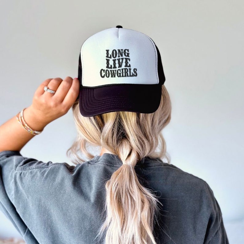 Op de afbeelding: Zwarte en witte truckercap met de tekst "Long Live Cowgirls" in zwarte letters.
