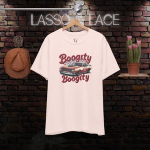 以下が含まれることがあります： 赤いレーシングカーのヴィンテージスタイルのグラフィックがプリントされたピンクのTシャツ。車の真上に「Boogitty」、真下に「Boogitty」と書いてあります。