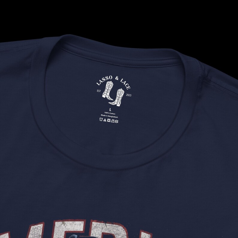 May include: A navy blue t-shirt with a white label that says "Lasso & Lace" with a pair of cowboy boots and the text "Est 2023". The label also says "100% Cotton Made in Bangladesh" and has a size label that says "L".