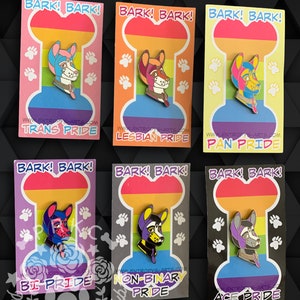 Puede incluir: Seis pines de esmalte con un perro de dibujos animados con diferentes banderas del orgullo. Los pines tienen todos el mismo diseño, pero cada uno tiene una bandera diferente: Orgullo Trans, Orgullo Lésbico, Orgullo Pan, Orgullo Bi, Orgullo No Binario y Orgullo Ace. Los pines están todos sobre un fondo blanco con un diseño de huella de pata.