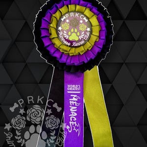 Könnte beinhalten: Eine mehrschichtige Rosette in Schwarz, Lila und Gold. Der Mittelteil zeigt einen transparenten Knopf mit einem Pfotenabdruck und Rosendesign, sowie den Text "Primrose Kennel Club". Lila und goldene Bänder sind angebracht, mit den Worten "Menace" und "World's Greatest".