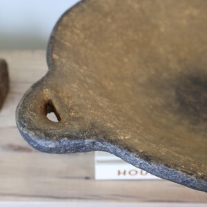 May include: Close-up of a rustic, brown, and gray decorative tray with a unique, scalloped edge and a small hole. The tray has a textured surface and appears to be made of stone or a similar material. The tray is a decorative item.