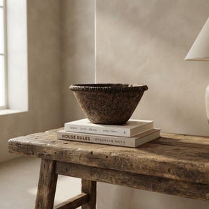 May include: A dark brown, textured, round bowl with a ridged rim sits atop two stacked books. The top book is titled House Love Home by Jenny Marrs, and the bottom book is titled HOUSE RULES by Myquillyn Smith, resting on a wooden bench.