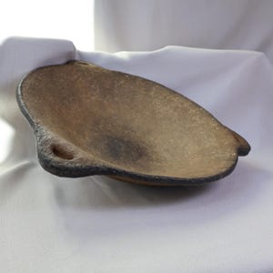 May include: A handcrafted, organic-shaped bowl with a textured, earthy brown surface and a dark, contrasting rim. The bowl features a small, circular opening on one side, adding a unique design element. The bowl is likely made of ceramic or a similar material.