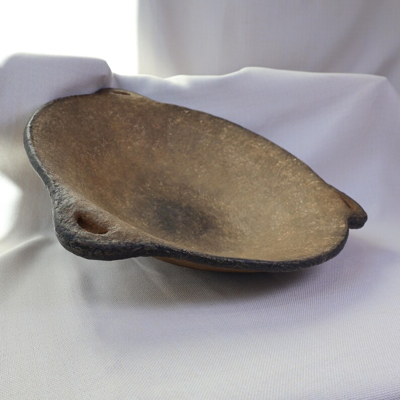 May include: A handcrafted, organic-shaped bowl with a textured, earthy brown surface and a dark, contrasting rim. The bowl features a small, circular opening on one side, adding a unique design element. The bowl is likely made of ceramic or a similar material.