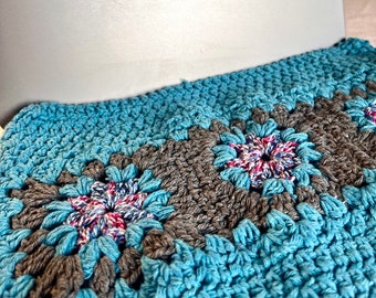 May include: A crocheted blanket with a blue and gray pattern. The blanket is made of squares with a flower design in the center of each square.