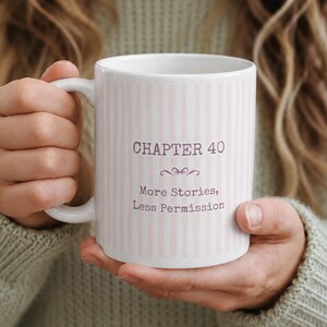 Peut inclure: Un mug en céramique blanche orné d'un motif à rayures verticales rose clair. Le texte "CHAPTER 40" est imprimé en gris foncé au-dessus d'une petite fioriture décorative, suivi du texte "More Stories, Less Permission" en gris foncé.