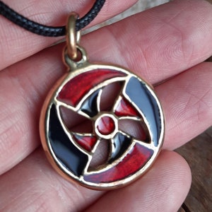 May include: A round pendant necklace with a black and red enamel design. The pendant features a cross shape with a red centre circle.