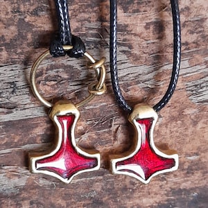 May include: Two red and gold Mjolnir pendants on black cords. The pendants are detailed with a red enamel finish and have a gold-toned metal loop at the top.
