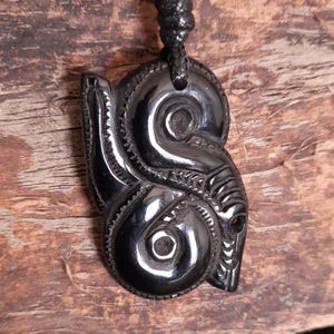 Può includere: Una collana con un ciondolo in legno nero intagliato con un design tradizionale Maori. Il ciondolo è in legno lucido e pende da un cordoncino nero.
