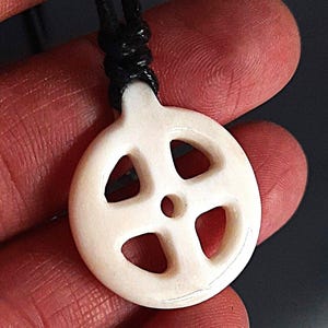 Può includere: Ciondolo in osso bianco con un design a nodo celtico intagliato, appeso a un cordoncino nero.