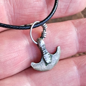 May include: A silver Viking axe pendant on a black leather cord. The axe features a detailed design and is a popular symbol of Norse mythology.