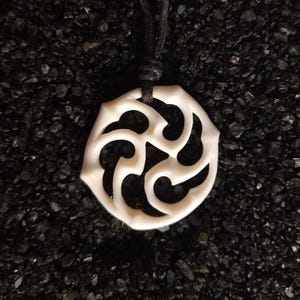 以下が含まれることがあります： 黒い紐に吊るされた、複雑な彫刻が施された白い骨のペンダント