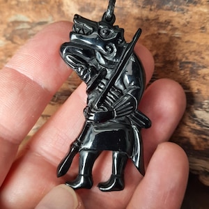 May include: Black obsidian pendant necklace featuring a detailed carving of a warrior holding a sword. The pendant is attached to a black cord.