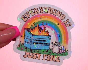 May include: A holographic sticker with a rainbow and a raccoon in front of a dumpster fire. The text reads "Everything is just fine" and "Emotional Dumpster Fire".