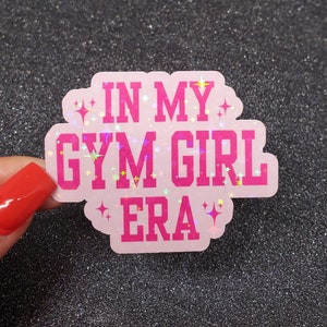 以下が含まれることがあります： 「In My Gym Girl Era」と書かれた、キラキラのアクセントが付いたピンクのステッカーです。