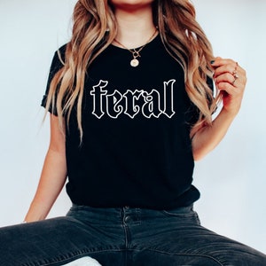Pu&ograve; includere: Una maglietta nera con un contorno bianco della parola "feral" in un font gotico.