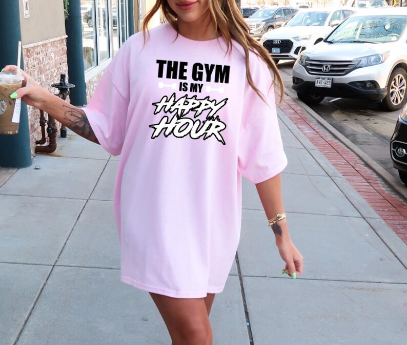 Peut inclure: Un t-shirt rose surdimensionn&eacute; avec le texte "The Gym is my Happy Hour" en noir et blanc. Le texte est dans une police de caract&egrave;res audacieuse et stylis&eacute;e.