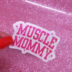 May include: A white sticker with pink glitter lettering that reads "MUSCLE MOMMY".