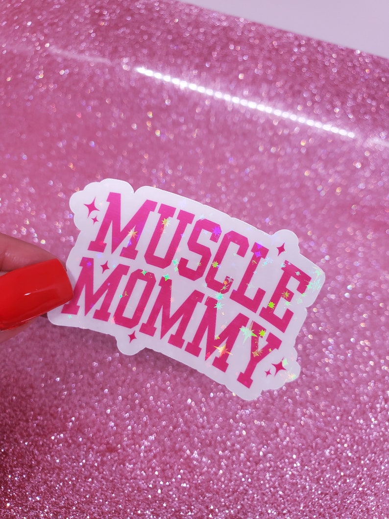 May include: A white sticker with pink glitter lettering that reads "MUSCLE MOMMY".